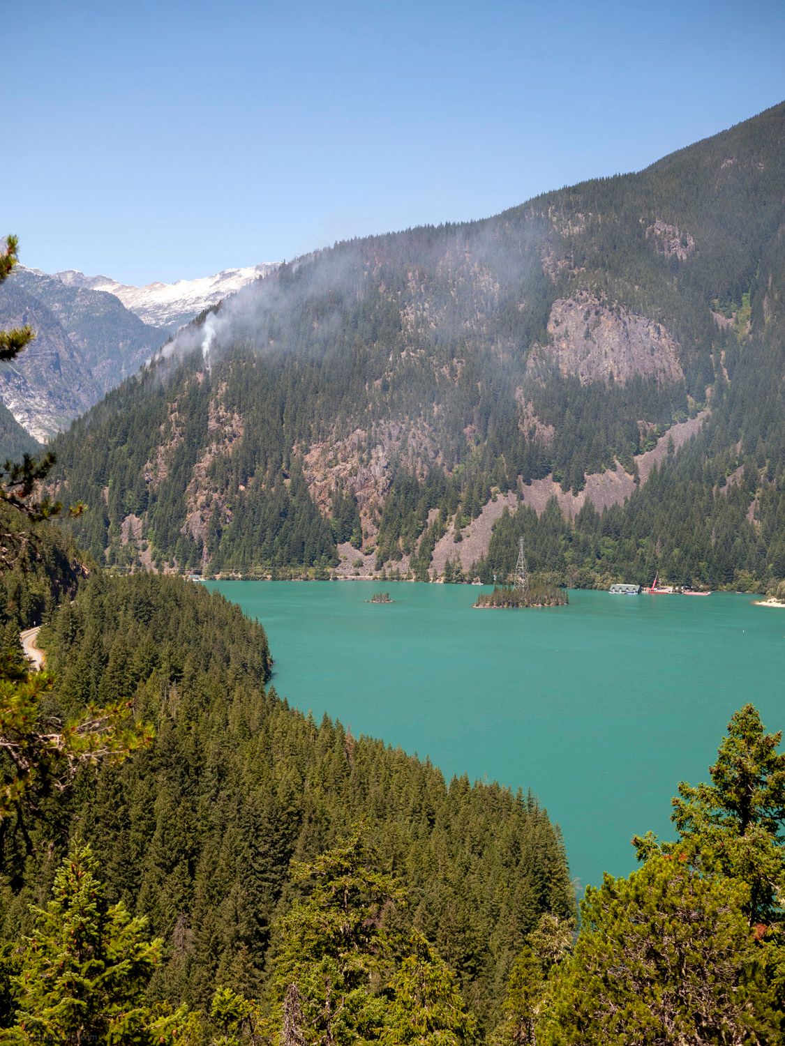 Landscape of a bright blue lake, with white smoke coming from the mountain in the center