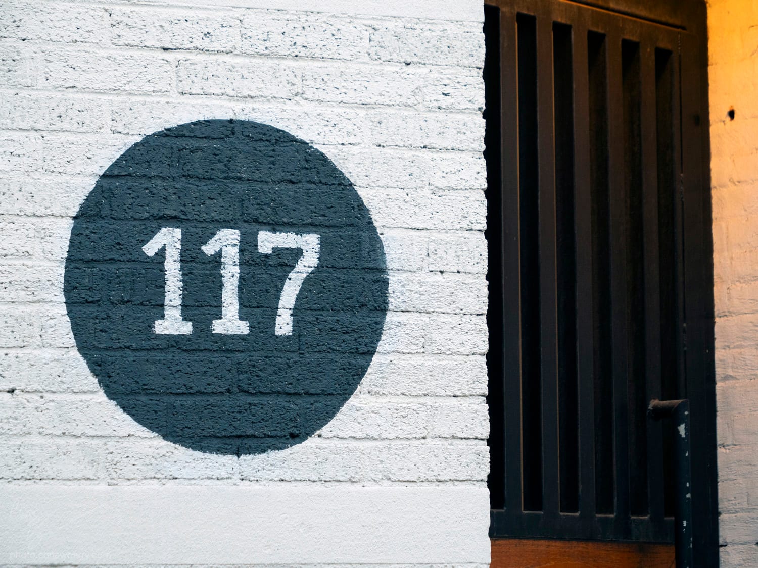 A white brick wall with a large black circle painted on it. In the middle of the circle are the numerals 117
